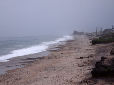 [Ocean waves coming from left to sand on right. House visible in distance through the fog.]